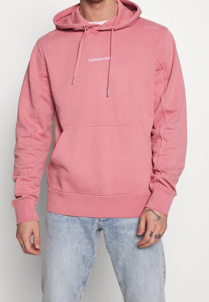 Felpa con cappuccio rosa con tasca a marsupio, coulisse e logo sul petto. Realizzata in tessuto morbido, con polsini e orlo a coste. Abbina jeans di denim chiaro.