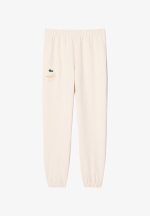 Pantalones deportivos de color crema con cintura y puños elásticos, que presentan un pequeño logo de cocodrilo verde y un detalle de garabato dorado en el muslo izquierdo.