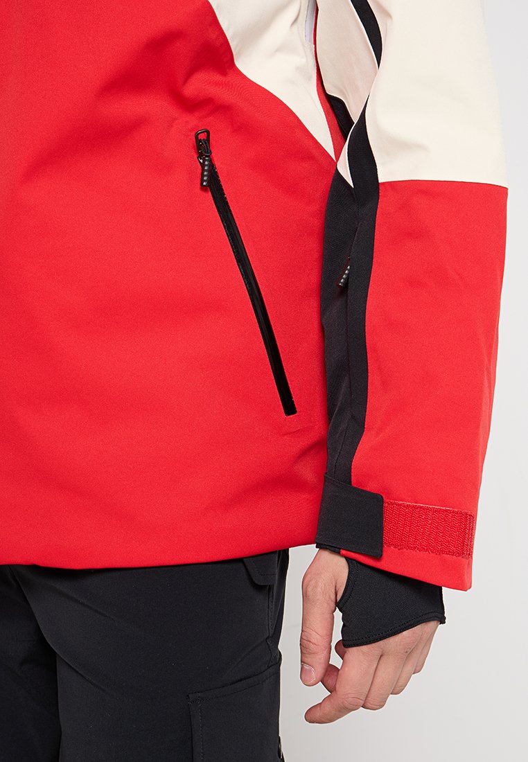 Rote Jacke mit schwarzem Reißverschlussfach, strukturiertem Stoff, weißen und schwarzen Akzenten sowie Klettverschlussärmelbündchen. Verfügt über ein sportliches, funktionales Design.
