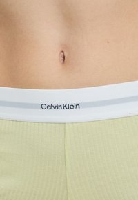 Light green ribbed fabric with a white waistband displaying "Calvin Klein" in black font. The waistband features two gray stripes.