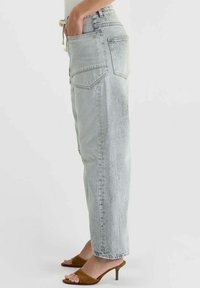 Jean gris clair taille haute avec cinq poches, coupe droite et légère décoloration. Associé à des sandales marron à talons.