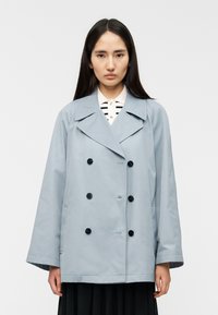 Φόρεμα διπλής όψης ανοικτού γαλάζιου χρώματος με μεγάλα μαύρα κουμπιά, φαρδύ γιακά και άνετη εφαρμογή. Λείο υλικό, χωρίς ορατά σχέδια ή διακοσμητικά στοιχεία.