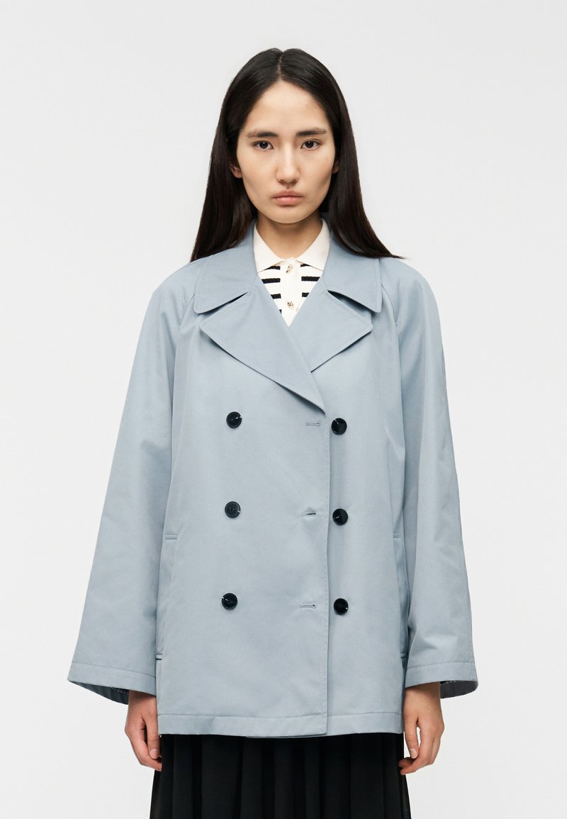 Φόρεμα διπλής όψης ανοικτού γαλάζιου χρώματος με μεγάλα μαύρα κουμπιά, φαρδύ γιακά και άνετη εφαρμογή. Λείο υλικό, χωρίς ορατά σχέδια ή διακοσμητικά στοιχεία.