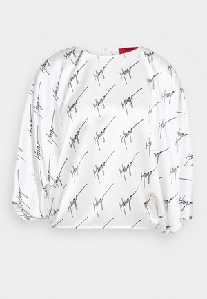 Vit långärmad blus med ett upprepat svart handskrivet "Hugo"-mönster, mjukt tyg och puffärmar med en subtil detalj vid halsringningen.