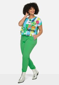 Korte mouwen, multicolor graphic t-shirt met blauwe, groene en roze patronen, gecombineerd met groene elastische broek en zilveren enkellaarsjes.