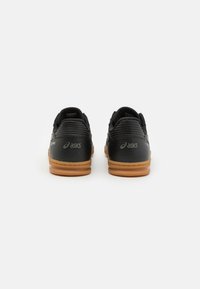 Scarpe da allenamento nere con tomaia in pelle testurizzata, suola in gomma a contrasto e logo Asics sul tallone. Design minimalista, vista posteriore.