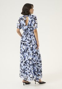 Robe maxi de couleur bleu clair avec un imprime floral noir et blanc. Manches courtes bouffantes, dos ouvert avec un détail de nouage, tissu fluide et coupe loose.