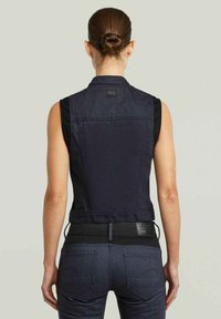 Gilet senza maniche in denim scuro con un design aderente, che mette in risalto un tessuto nero a contrasto sulle spalle e una patch con il marchio sul retro.