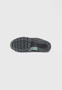 Black athletic shoe outsole with textured rubber, featuring a green accent. Tread pattern includes rectangular and oval indentations for grip.