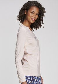Light pink long-sleeve t-shirt with a rounded neckline and side seam detailing. Paired with patterned blue bottoms. Smooth texture.