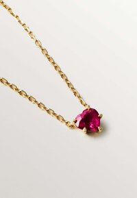 Collar de cadena dorada que presenta una piedra rosa en forma de corazón, con cuatro engastes de garra asegurando la gema. Metal pulido y textura suave.