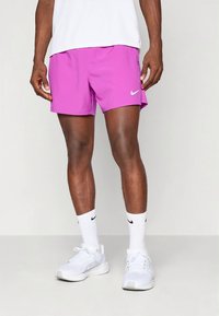 Calções desportivos masculinos da Nike em rosa vivo, tecido de poliéster, cintura elástica, textura suave, combinados com meias e sapatos brancos da Nike.