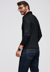 Sort langærmet polo skjorte set bagfra, parret med mørkeblå denim jeans. Har en glat tekstur, enkelt design og minimale detaljer.