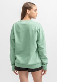 Felpa verde menta con scollo rotondo, maniche a costine e orlo a costine. Presenta un logo discreto sopra lo scollo e una vestibilità rilassata.