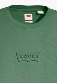 Zöld pamut póló, laza fazonnal, bordázott kerek nyakkal és domború Levi's logóval az elején. Egyszerű és textúrált anyag.