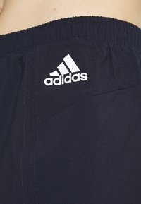 Pantalones cortos deportivos de color azul marino hechos de tela ligera con una cinturilla elástica. Presentan un logo de Adidas en blanco en la parte superior.