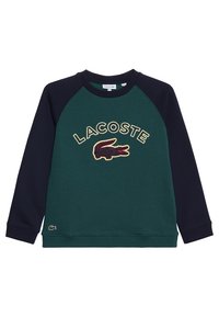 Felpa in pile verde e blu con maniche raglan, caratterizzata da un prominente logo ricamato "LACOSTE" e l'emblema di un coccodrillo sul fronte.