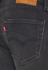 Gros plan sur la poche arrière d'un jean en denim noir avec l'étiquette rouge Levi's visible et un patch de marque en cuir marron au-dessus de la ceinture.
