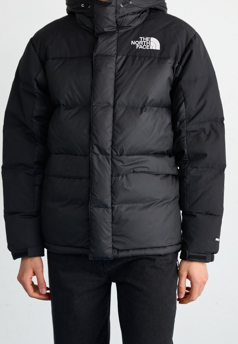 Chaqueta acolchada negra aislante con cierre delantero, capucha y logo. Confeccionada con un material suave y ligero, presenta segmentos de corte cuadrado.