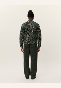 Floral-printed jacket in dark green with red and orange accents, paired with dark green trousers. Features a relaxed fit and long sleeves.