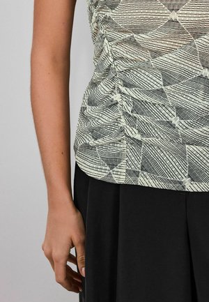 Top leggero e decorato con motivi geometrici in nero e crema. Presenta un tessuto strutturato con i lati arricciati, abbinato a una gonna nera.