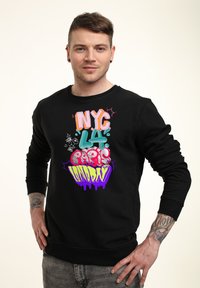 Sudadera negra con texto al estilo graffiti colorido, que incluye "NYC", "PARÍS" y "LONDRES", con tonos llamativos como rosa y púrpura.