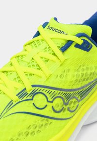 Bright yellow athletic shoe with mesh material, blue accents, and flat laces. Features a logo and a textured sole design.