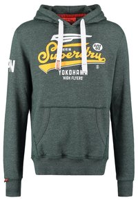 Sudadera de color verde oscuro de Superdry con cordones blancos, bolsillo frontal tipo canguro y logo amarillo y blanco "Superdry Yokohama High Flyers" en el frente.