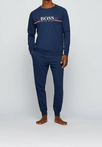 Conjunto de loungewear en azul marino que incluye un sudadera con el gráfico "BOSS HUGO BOSS" y detalles a rayas, complementado con pantalones ajustados a juego.
