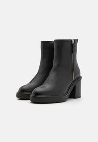 Botas negras de tobillo hechas de cuero texturizado, con un tacón grueso, cremallera lateral y una suela de plataforma de goma para mayor altura.