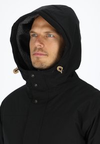 Black hooded jacket with a soft, textured interior. Features button closures and adjustable drawstrings near the collar.
