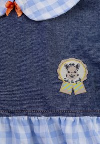 Vestito di jeans con colletto a quadri blu e bianchi, caratterizzato da un orlo arricciato e una patch con un giraffa sorridente su un nastro.