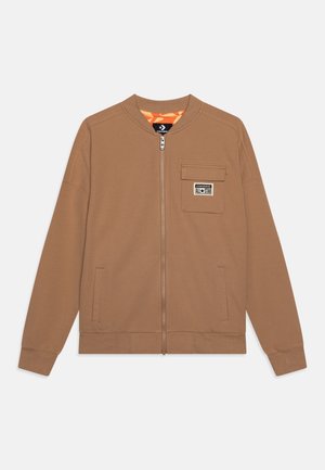 Veste zippée marron clair avec poignets côtelés, deux poches avant et un patch "Converse All Star" sur la poche poitrine.