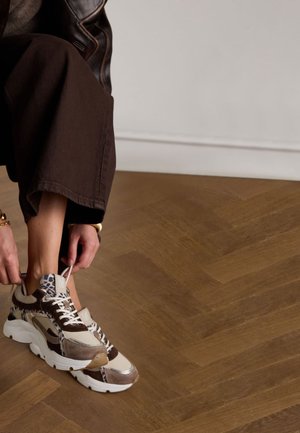 Baskets chunky avec des accents imprimés animaliers marron, beige et bleu, dotées de lacets blancs et d'une épaisse semelle blanche, sur un sol en bois.