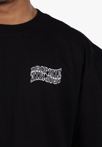 Zwarte katoenen t-shirt met een vervormd wit tekstontwerp met de tekst "DROPSIZE" op de linkerkant van de borst. Korte mouwen en ronde hals.