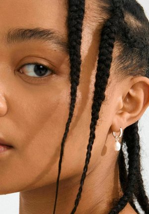Silberner Creolenohrring mit strukturiertem Design und einem Perlenakzent. Trägt das Modell am Ohr und zeigt seine runde Form und den glänzenden Finish.