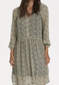 Robe légère et fluide en tissu doux et transparent. Caractérisée par un motif abstrait noir sur fond beige, avec un devant à boutons et des manches 3/4.