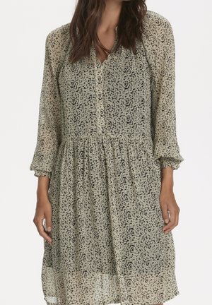 Robe légère et fluide en tissu doux et transparent. Caractérisée par un motif abstrait noir sur fond beige, avec un devant à boutons et des manches 3/4.