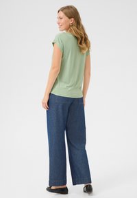 Haut vert à manches courtes associé à un pantalon en denim bleu à jambes larges. Le haut a une coupe décontractée et une texture lisse ; le pantalon présente des détails de couture.