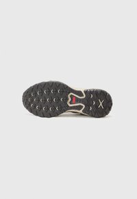 Suela de goma negra con patrones de agarre texturizados, con acentos crema y un logotipo rojo prominente. Diseñada para ofrecer tracción y durabilidad.
