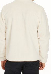 Chaqueta de forro polar color crema con una superficie suave y texturizada, que presenta un corte holgado y mangas largas, ideal para un uso informal.