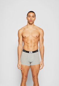 Pilki medvilniniai bokseriai su juodu juosmeniu, ant kurio yra "Calvin Klein" logotipas, sukurti prigludusiai siluetai.