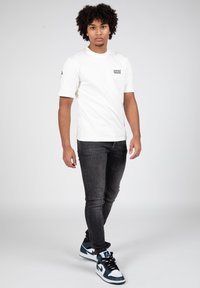 Camiseta blanca de manga corta con el texto negro "AMIGOS INCORRECTOS", combinada con jeans skinny oscuros y zapatillas altas azul y blancas.