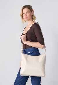 Beige woven handbag with a smooth texture, slouchy shape, and adjustable strap, featuring subtle gold-tone hardware accents.