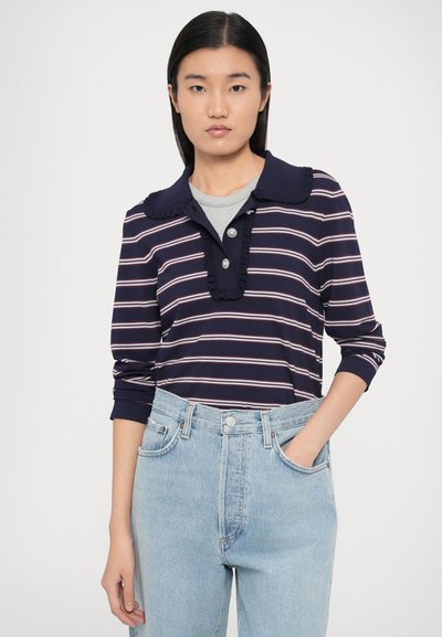 Granatowo-biała koszulka polo w paski z długim rękawem, z falbankowym kołnierzykiem i zdobieniem na guziki, w połączeniu z jasnoniebieskimi, wysokim stanem dżinsami.
