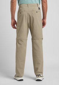 Beige Reißverschluss-Hosen aus leichtem Material, mit flachem Bund, zwei Gesäßtaschen und sichtbaren Nähdetails.