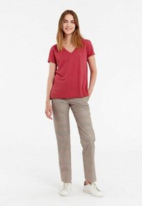 T-shirt rouge à col en V associé à un pantalon à carreaux et des baskets blanches. Le T-shirt a des manches courtes et le pantalon a une coupe ajustée.