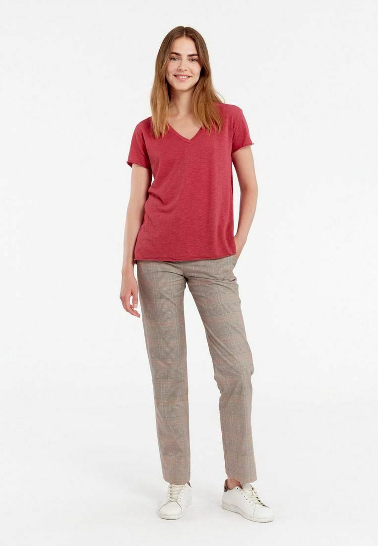 T-shirt rouge à col en V associé à un pantalon à carreaux et des baskets blanches. Le T-shirt a des manches courtes et le pantalon a une coupe ajustée.