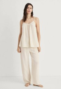Lichte, ribbelige crèmekleurige pyjama's met een losse tanktop en wijde broekspijpen. Verstelbare spaghettibandjes en een zachte textuur.