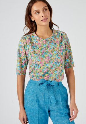 Top con stampa floreale a maniche corte, caratterizzato da fiori rosa, blu e arancioni su uno sfondo chiaro. Abbinato a pantaloni blu a vita alta.